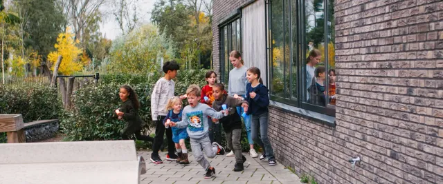 Groep kinderen rent met Picoo-controllers langs een schoolgebouw